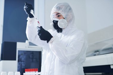 Biyolojik tehlike giysisi ve solunum cihazında ciddi konsantre sağlık bilimcisi laboratuvarda durarak ve virüs örneğini test ederken kan bırakarak
