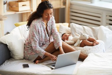 Pamuk gömlek yatakta oturan ve dizüstü bilgisayarda yazarak içerik çoklu görev genç Afrikalı anne ise bebek çocuk Koza yatarken