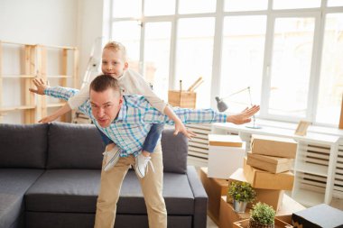 Yeni düz onunla uçak oynarken damalı gömlek içinde pozitif yakışıklı genç baba silah tutarak ve oğul piggyback binmek vererek