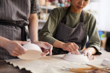 Çömlek atölyesinde çalışırken kil tabakları parlatmak için züppesi kullanarak önlükteki meşgul kadınların yakın çekim