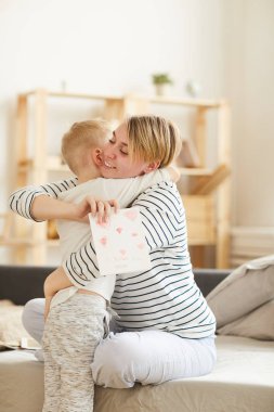 Sabah ona el yapımı kart vererek anne sıkı sarılırken sevimli çocuk seven, yatakta oturan heyecanlı anne ve mevcut mutlu olmak