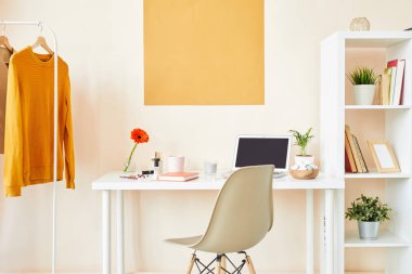 Duvar, beyaz sandalye, eşyalar ile mobilya ve askı üzerinde giyim ile masa ile yaratıcı çalışan veya tasarımcı iş yeri