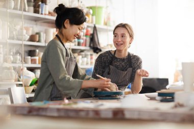 Seramik stüdyosunda çalışırken masada oturup sohbet önlükpozitif çekici genç çok ırklı çömlekçiler