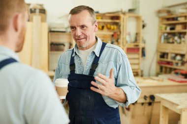 Atölyede kahve molası sırasında işçi ile konuşan kıdemli marangoz portresi, kopya alanı