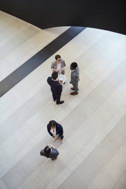 Şirket lobisinde duran ve birbirleriyle sohbet eden formalwear çok ırklı iş arkadaşlarının doğrudan yukarıda görünümü