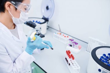 Beyaz önlük ve kauçuk eldiven ciddi meşgul genç kadın laboratuvar işçisi masada duran ve numuneler ile çalışırken test tüpükan ekleme