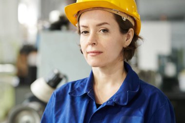 Fabrikada poz verirken kameraya bakan hardhat giyen kendine güvenen kadın işçinin baş ve omuz portresi, kopya alanı
