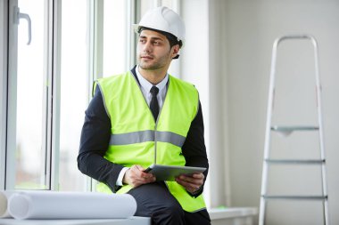 Şantiyede pencereye bakan hardhat giyen Orta Doğulu işadamının bel den yukarı portresi, kopya alanı