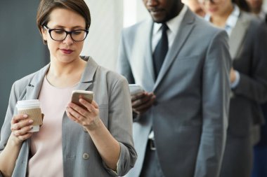 Kısa saçlı, kısa saçlı ve akıllı telefondaki sms'leri kontrol ederken kahve içen içerik dalgın iş kadını