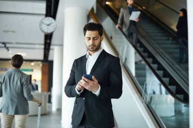 Havaalanı salonunda duran sakallı ciddi meşgul yakışıklı genç işadamı uçuş programı kontrol ederken gadget üzerinde internet tarama