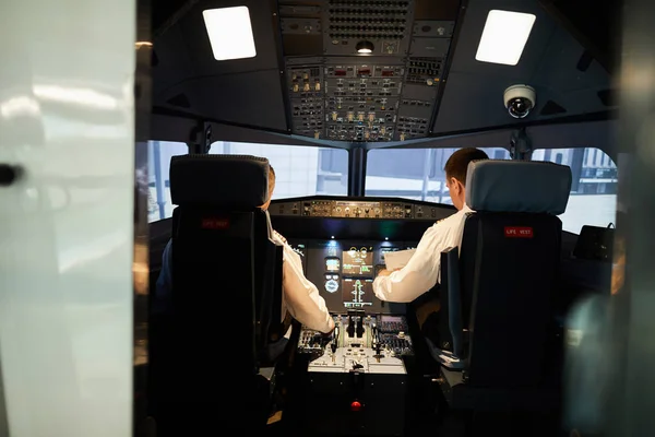 Widok Tyłu Poważnych Pilotów Białych Koszulkach Siedzących Panelach Sterujących Pokrętłami — Zdjęcie stockowe
