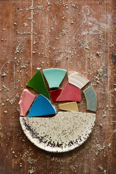 High angle view of multi-colored puzzles of ceramic plate on dirty scratched table with clay dust, copy space