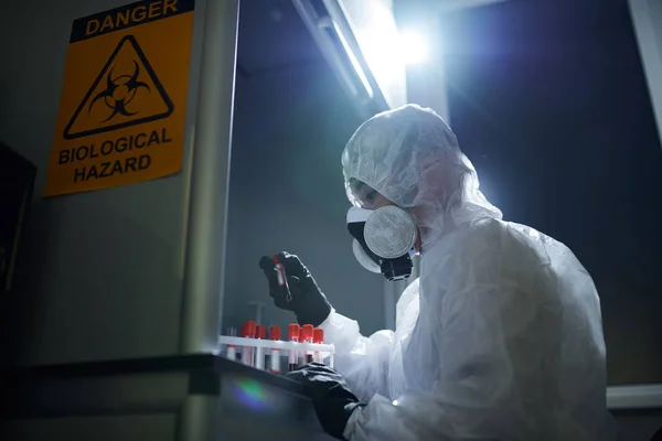 在暗室进行研究时 身着生物危害服和呼吸器的严重浓缩微生物学家检查危险样品 — 图库照片