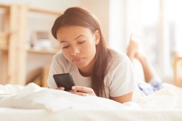 Retrato Bela Mulher Raça Mista Usando Smartphone Deitado Cama Iluminado — Fotografia de Stock