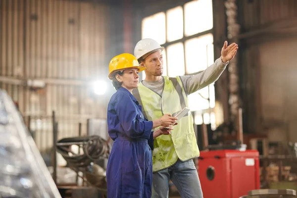 Portrait of two workers discussing production standing in indusrial workshop and pointing up, copy space