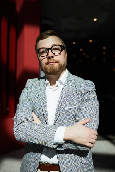 Portrait of pensive confident chubby businessman with beard wearing glasses standing in dark room
