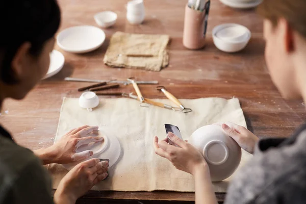 Rear view of unrecognizable craftswomen sitting at old wooden table and polishing clay dishes with sandpapers in workshop — Stock Image Rear View Unrecognizable Craftswomen Sitting Old Wooden Table Polishing Clay Stock Photo