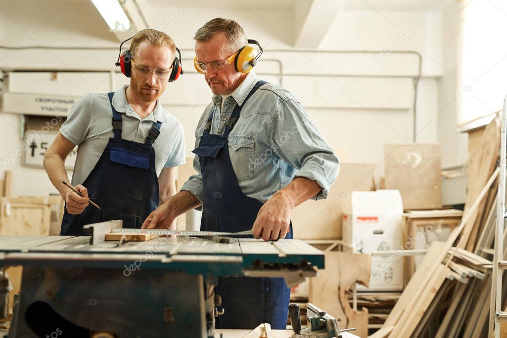 Waist up  portrait of senior carpenter working with apprentice in joinery workshop, copy space