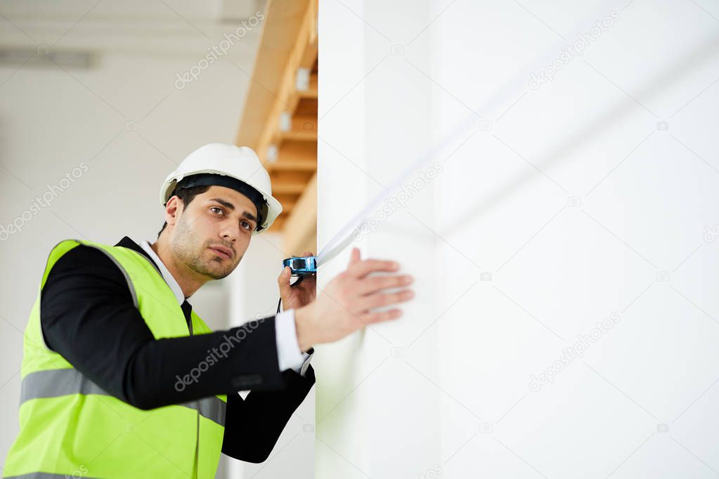 Low angle portrait of handsome Middle-Eastern engineer measuring walls at construction site, copy space
