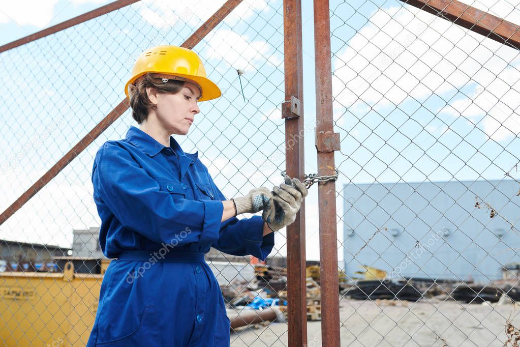 Portrait of female worker closing gates of construction site and locking padlock with keys, copy space