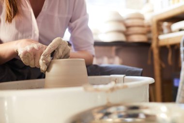 Stüdyoda çalışırken çömlekçi tekerleğinde kil şekillendiren kadın ellerinin yan görünümü, kopya alanı