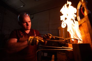 Genç demirci fırında çelik parça ısıtma sırasında sıcak sıcaklıktan kaşları kaşları