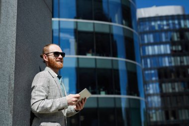 İş bölgesinde duran ve tablet üzerinde online veri ile çalışan hipster giyim gülümseyen girişimci genç yönetici