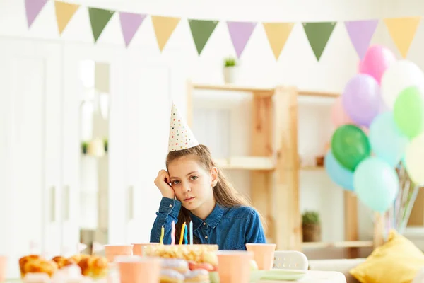 Portrait of sad teenage girl sitting alone at party table in decorated room, copy space