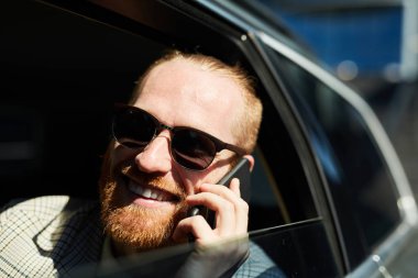 Neşeli memnun hipster kırmızı sakallı genç işadamı otomobil içinde oturan ve telefonda iyi haber alıyor