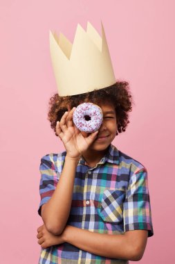 Waist up portrait of smiling African-American boy holding donut posing against pink background, Birthday party concept clipart