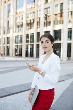 Akıllı telefonu tutan ve iş alanında açık havada poz verirken kameraya bakan güzel genç kadının portresi, kopya alanı