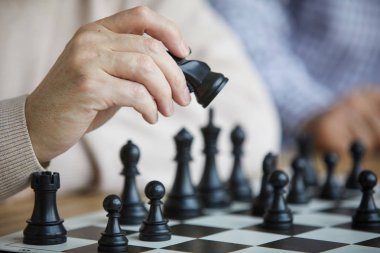 Bej kazak eski satranç oyuncusunun kırışık eli satranç tahtası boyunca siyah satranç figürü hareket