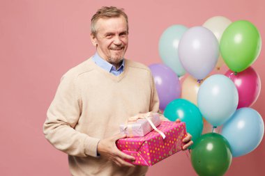Çok renkli balonlar ile pembe arka plan karşı duran ve doğum günü hediyeleri tutan kazak Neşeli yakışıklı olgun sakallı adam