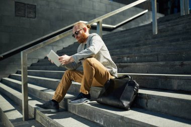 Merdivenlerde oturan ve tablet online rapor analiz güneş gözlüğü Ciddi modern sakallı yöneticisi