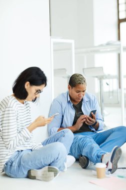 Sosyal medyada gezinirken yerde oturan ve akıllı telefon kullanan yoğunlaştırılmış mobil genç çok ırklı öğrenciler