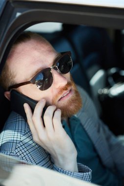 Gülümseyen pensive hipster sakallı işadamı güneş gözlüğü içinde araba içinde telefonda konuşurken yer arıyor