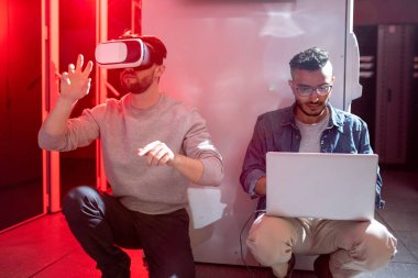 Ciddi meraklı genç çok ırklı It mühendisleri veri merkezinde katta oturan ve artırılmış gerçeklik için yeni uygulama test