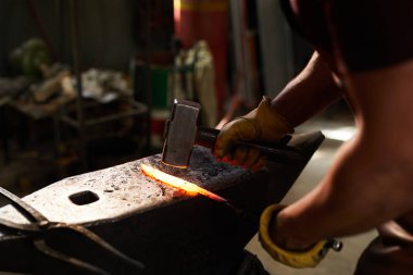 Çelik örste duran ve atölyede çekiçle ısıtmalı metal çubuğu şekillendiren tanınmayan demircinin yakın çekim