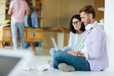 Birlikte internet kaynaklarını analiz ederken rahat giyim meşgul genç meslektaşları birlikte çalışma alanında katta oturan ve dizüstü bilgisayar kullanarak