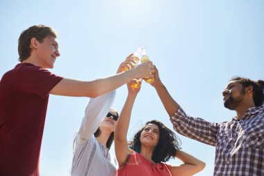 Yaz aylarında mavi gökyüzüne karşı bira şişeleri clinking arkadaşlar düşük açı portre, uzay kopyalamak