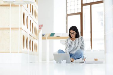 İnternette veri kontrol ederken kütüphanede yerde çapraz bacaklar ile oturan ve dizüstü bilgisayar kullanarak gözlük konsantre modern kadın pazarlama uzmanı