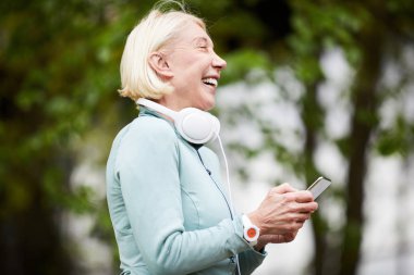 Yaz gününde doğal ortamda kaydırma veya mesajlaşma sırasında akıllı telefon gülme ile Olgun kendinden geçmiş sporcu