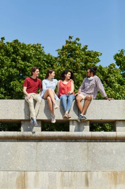 Köprüde oturan ve mutlu Yaz zevk sohbet gençlerin bir grup, kopya alanı