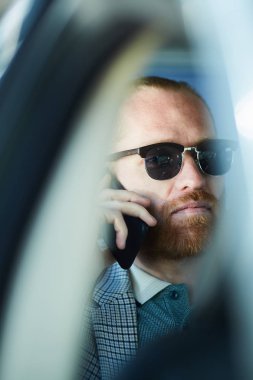 Araba içinde oturan ve telefonda iş sorunları çözme güneş gözlüğü ciddi düşünceli sakallı girişimci