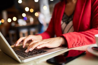 Blog için makale yazarken kırmızı ceketli tanınmayan siyah kadının yakın çekim masada oturup dizüstü bilgisayarda yazarak