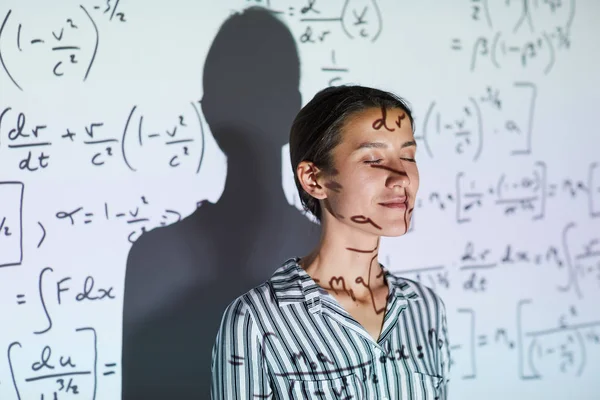 内容平静的年轻女士在上衣站在投影屏幕与数学公式和保持眼睛闭上大学课 — 图库照片