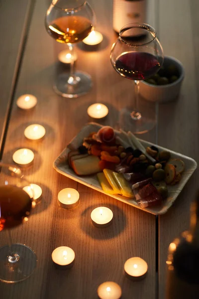 High angle closeup of romantic dinner with wine glasses and snacks on wooden table lit by candle light, copy space