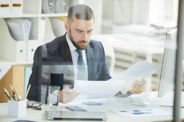 Joven Hombre Negocios Barbudo Serio Traje Sentado Mesa Examinando Documentos — Foto de Stock