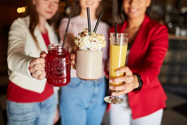 Close-up of young women reaching hands with refreshing cocktails for party to camera while having fun together