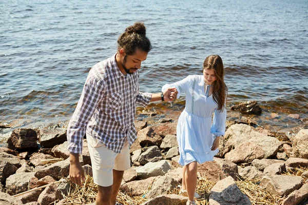 Portrait of young interracial couple climbing rocky beach by sea, copy space